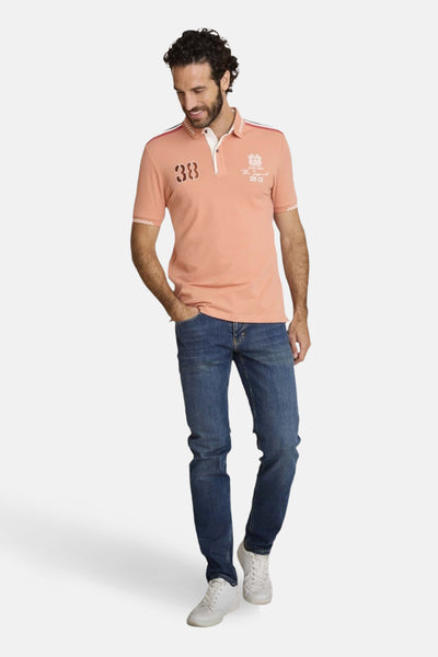 Polo à manches courtes orange de DELAHAYE avec rayures décoratives, porté avec un jean bleu et des baskets blanches.