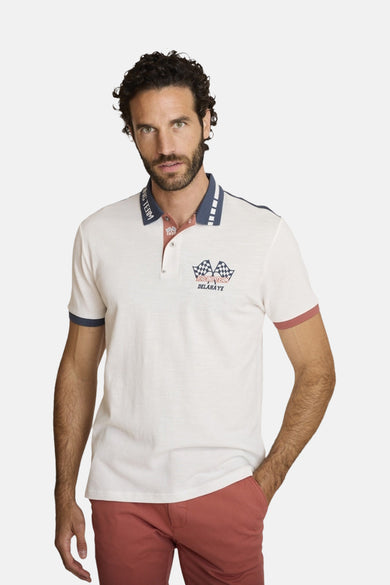 Polo écru à manches courtes de DELAHAYE, col et manches contrastés, motif imprimé sur la poitrine, porté avec un pantalon rouge.
