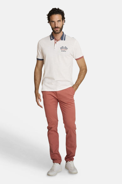Polo écru à manches courtes par DELAHAYE, avec motif de course et porté avec un pantalon corail et des chaussures blanches.