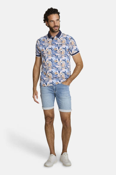 Polo bleu de DELAHAYE, à motif de feuilles exotiques et manches courtes, porté avec un short en jean et des baskets blanches.
