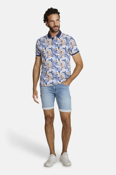 Polo bleu de DELAHAYE, à motif de feuilles exotiques et manches courtes, porté avec un short en jean et des baskets blanches.
