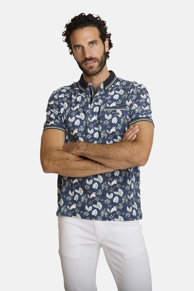 Polo bleu de DELAHAYE, à motifs floraux, porté avec un pantalon blanc.