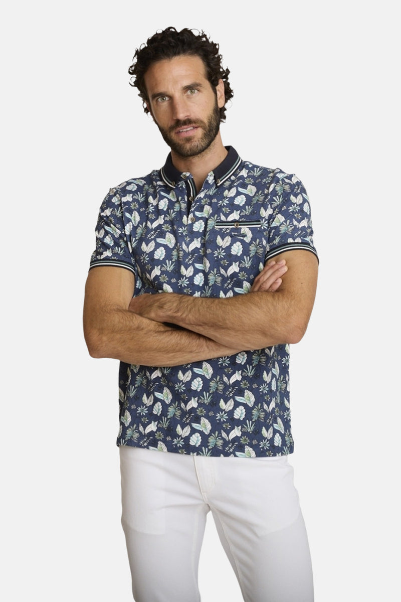 Polo bleu de DELAHAYE, à motifs floraux, porté avec un pantalon blanc.