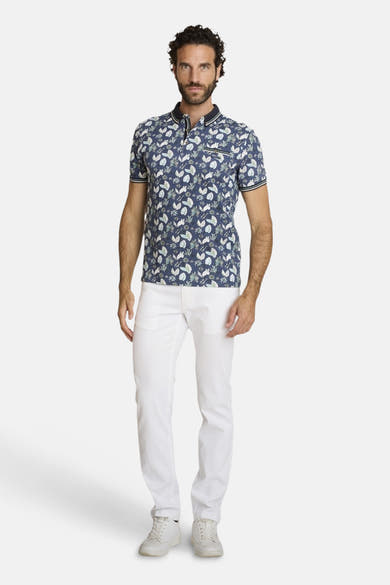 Polo bleu par DELAHAYE, avec un motif floral, porté avec un pantalon blanc et des baskets blanches.