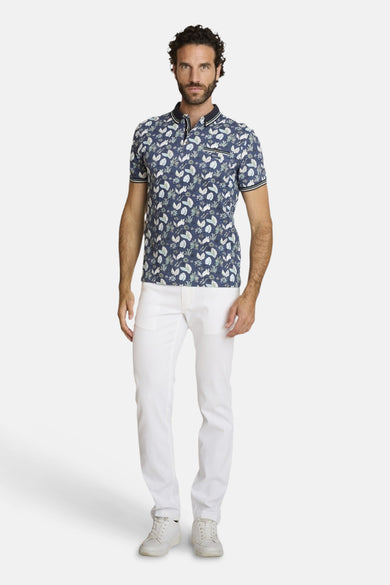 Polo bleu par DELAHAYE, avec un motif floral, porté avec un pantalon blanc et des baskets blanches.