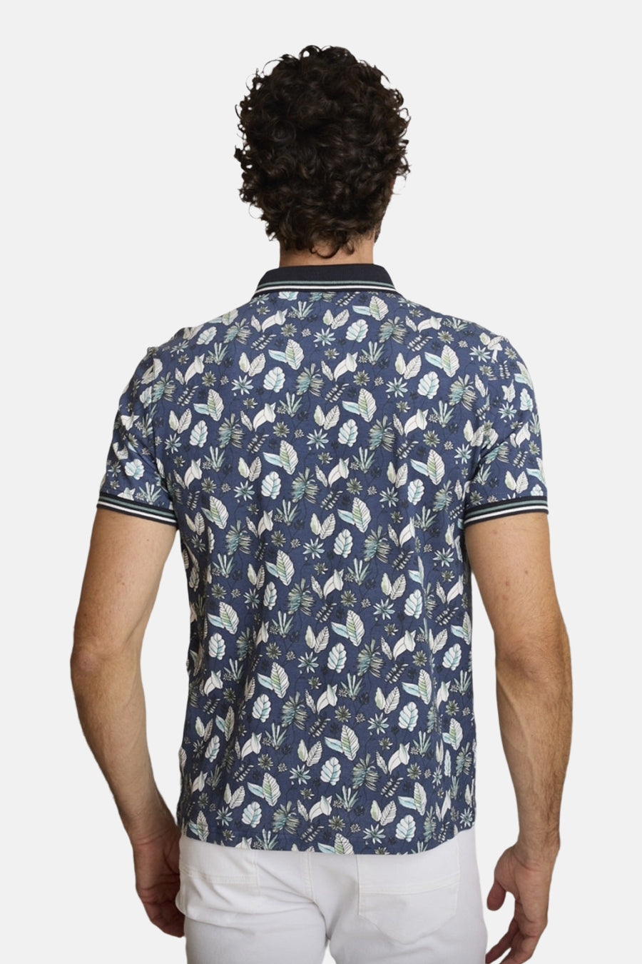 Polo bleu de DELAHAYE, imprimé avec motifs de feuilles, vu de dos, porté avec un pantalon blanc.
