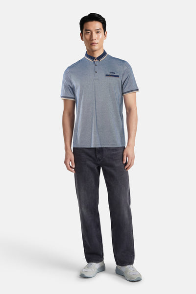 Polo bleu de DELAHAYE, avec détails contrastants au col et à la poche poitrine, porté avec un jean et des baskets gris.