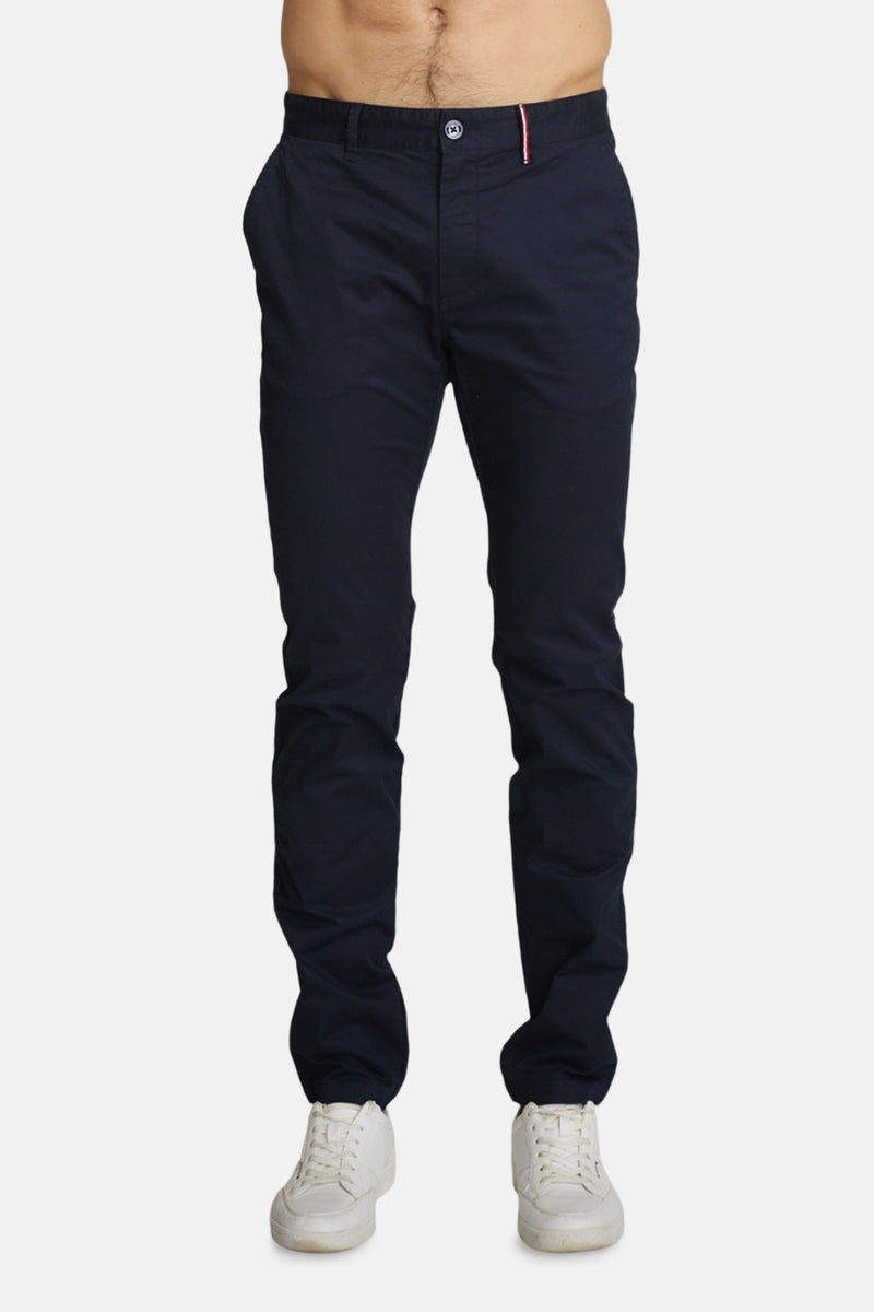 Marineblauwe chino van DELAHAYE, met roze biezen op de achterzakken, gedragen met witte sneakers.
