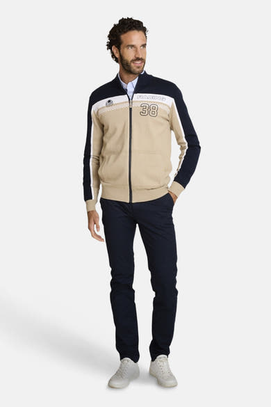 Marineblauwe chino van DELAHAYE, gedragen met een beige en wit gestreepte jas met rits en witte sportschoenen.