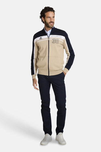 Marineblauwe chino van DELAHAYE, gedragen met een beige en wit gestreepte jas met rits en witte sportschoenen.