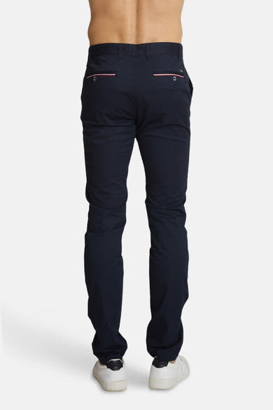 Chino bleu marine de DELAHAYE, avec passepoils roses sur les poches arrière, porté avec des baskets blanches.