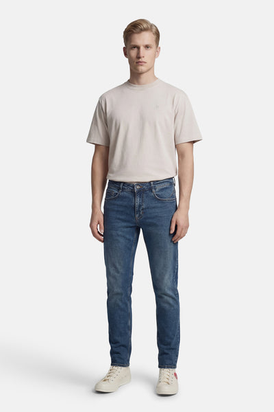 Jean droit bleu de DELAHAYE, porté avec un t-shirt beige et des baskets crème à motif cœur rouge.