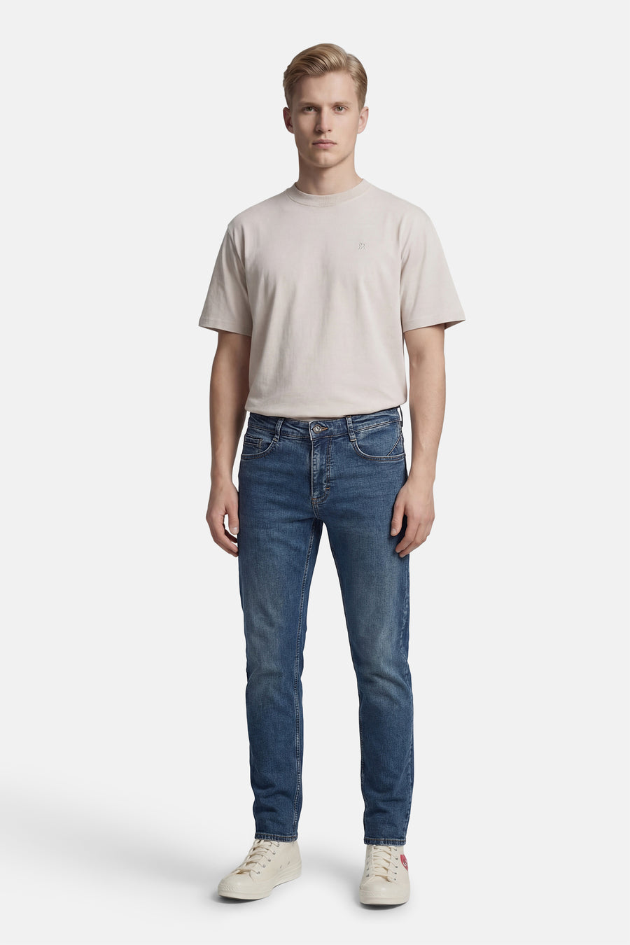 Jean droit bleu de DELAHAYE, porté avec un t-shirt beige et des baskets crème à motif cœur rouge.