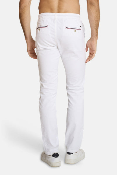 Chino blanc de DELAHAYE, avec des poches arrière passepoilées à rayures, porté avec des baskets blanches.