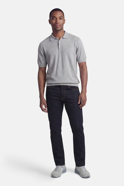 Jean droit en denim bleu foncé de DELAHAYE, porté avec un polo gris et des baskets grises.

