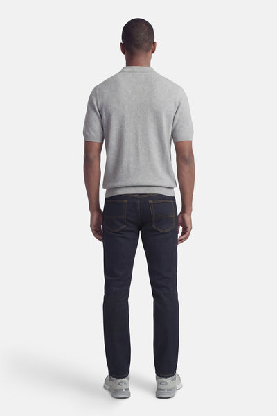 Jean droit bleu foncé en denim de DELAHAYE, porté avec un polo gris côtelé et des baskets grises.