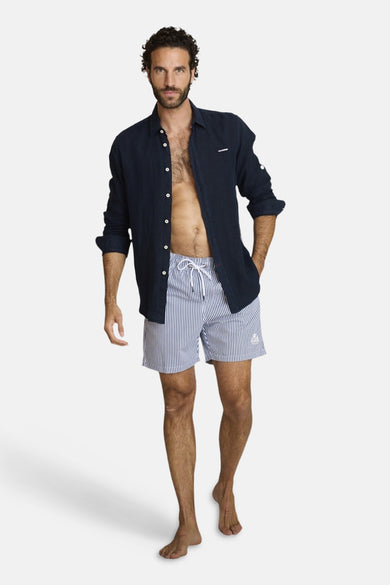 Multicolored striped men's swim shorts with white drawstring and side pocket, worn with navy button-up shirt, full-length front view