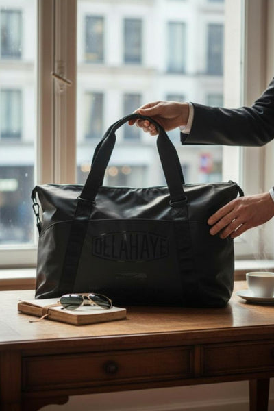 Black leather shoulder bag by Delahaye with embossed logo, shown on wooden table in lifestyle setting