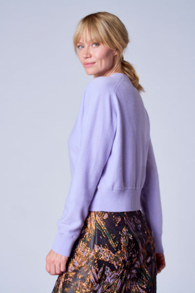 Paarse TERRE BLEUE gilet gedragen met een abstracte rok, blonde vrouw die over haar schouder kijkt.