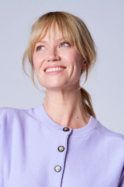 Gilet violet de TERRE BLEUE, avec boutons décoratifs dorés, porté par un modèle souriant avec des cheveux blonds.
