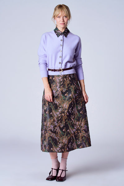 Gilet violet par TERRE BLEUE, porté avec une jupe à motifs et des chaussures à brides.
