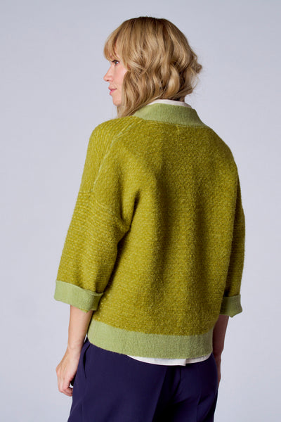 Gilet vert par TERRE BLEUE, manches trois-quarts, texture bouclée, porté avec un pantalon bleu marine.