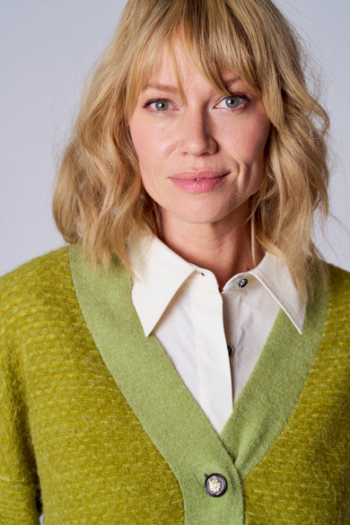 Gilet vert de TERRE BLEUE avec bouton décoratif, porté sur une chemise blanche à col.
