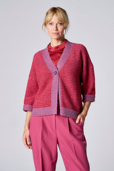 Gilet violet de TERRE BLEUE, tricoté avec motif texturé, porté sur un chemisier rouge et un pantalon rose assorti.
