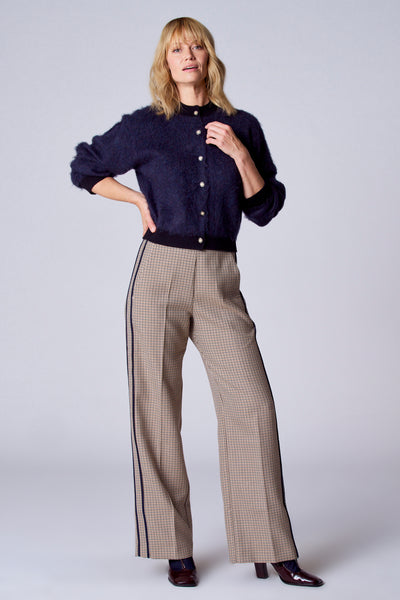 Gilet bleu de TERRE BLEUE, porté avec un pantalon à carreaux à rayures et des chaussures bordeaux à talons.