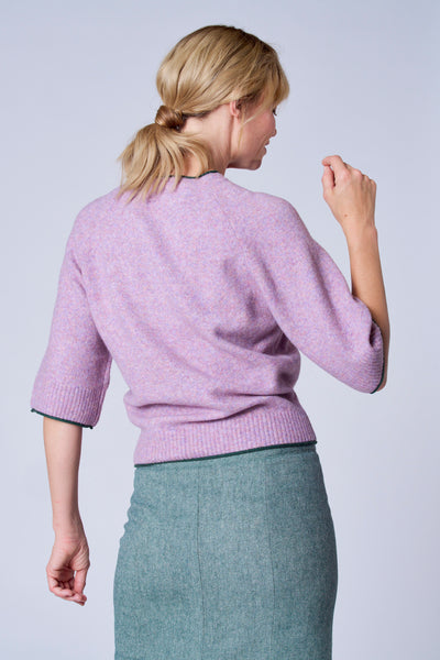 Pull violet par TERRE BLEUE avec bordure verte, porté avec une jupe crayon texturée.