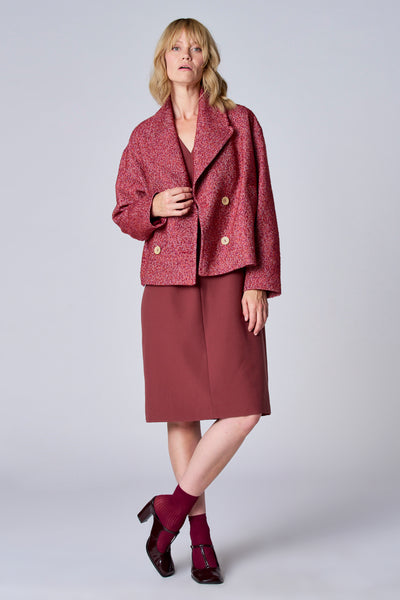 Veste courte rouge de TERRE BLEUE, texturée, avec une robe et des chaussures bordeaux portées par le modèle.
