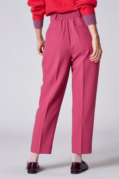 Short rose de TERRE BLEUE, coupe tailleur, porté avec un pull en maille rouge et des chaussures vernies bordeaux.