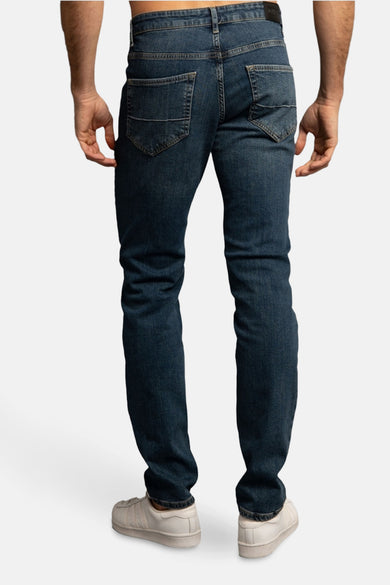 Jean en denim bleu foncé divers pour hommes de DELAHAYE, avec poches arrière et chaussures blanches.