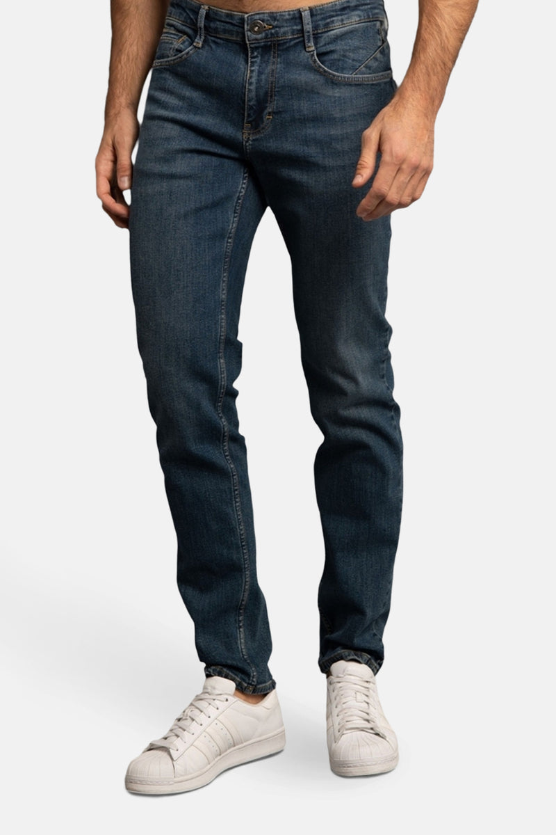 Jean bleu foncé en denim, de DELAHAYE, porté avec des baskets blanches.