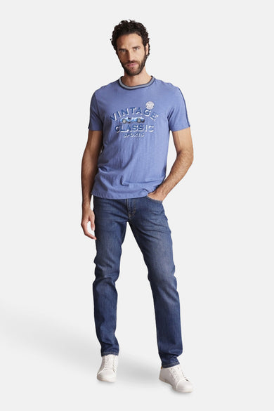 Blauwe T-shirt met korte mouwen van DELAHAYE, met opdruk van een oldtimer, gedragen met een spijkerbroek en witte sneakers.