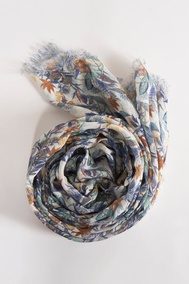 Foulard multicolore de DELAHAYE avec motif floral et détails frangés, enroulé sur un fond clair.
