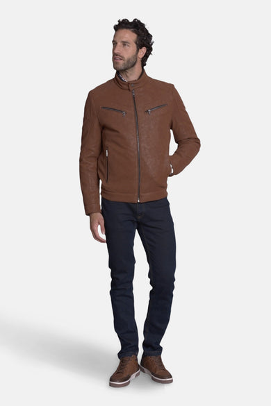 Veste courte en cuir brun de DELAHAYE, avec fermeture éclair et poches zippées, portée avec un jean bleu et des baskets marron.
