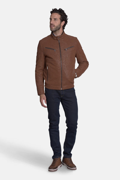 Veste courte en cuir brun de DELAHAYE, avec fermeture éclair et poches zippées, portée avec un jean bleu et des baskets marron.