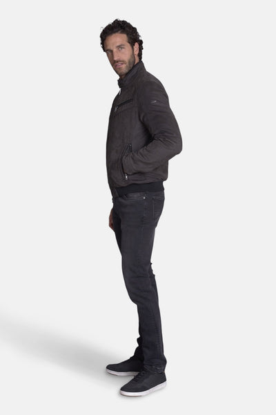 Veste courte brune en cuir par DELAHAYE, avec fermeture éclair et poches, portée avec un jean noir et des baskets.
