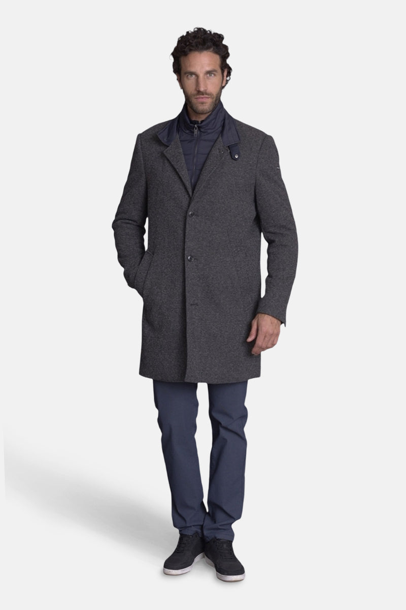 Lange grijze jas van DELAHAYE, gedragen met een marineblauwe gilet en een bijpassende broek.