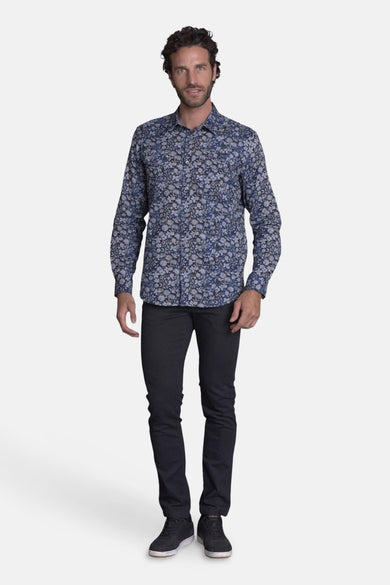 Blauwe DELAHAYE blouse met bloemenpatroon, gedragen met een antracietkleurige broek en zwarte schoenen.