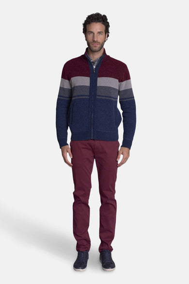 Multikleuren gebreid vest van DELAHAYE, met horizontale strepen, gedragen met een bordeauxrode broek en blauwe schoenen.