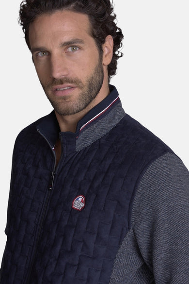 Gilet matelassé bleu de DELAHAYE, avec empiècements en tissu texturé gris sur les épaules et le col.