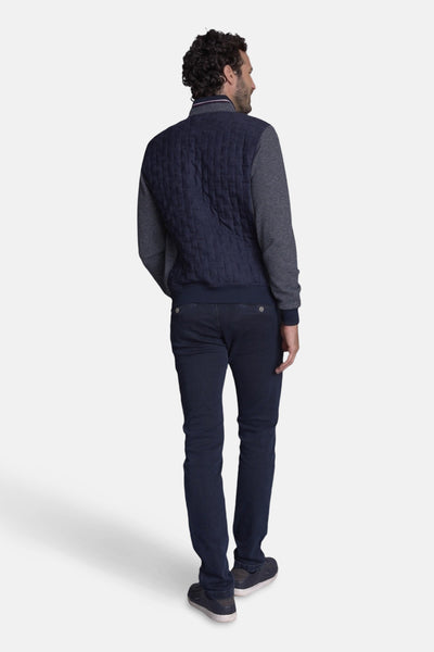 Gilet bleu marine matelassé par DELAHAYE, avec des manches gris chiné, porté avec un jean et des baskets bleues.