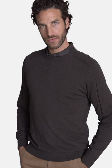 Pull col rond brun de DELAHAYE, porté avec une chemise à pois et un pantalon beige.