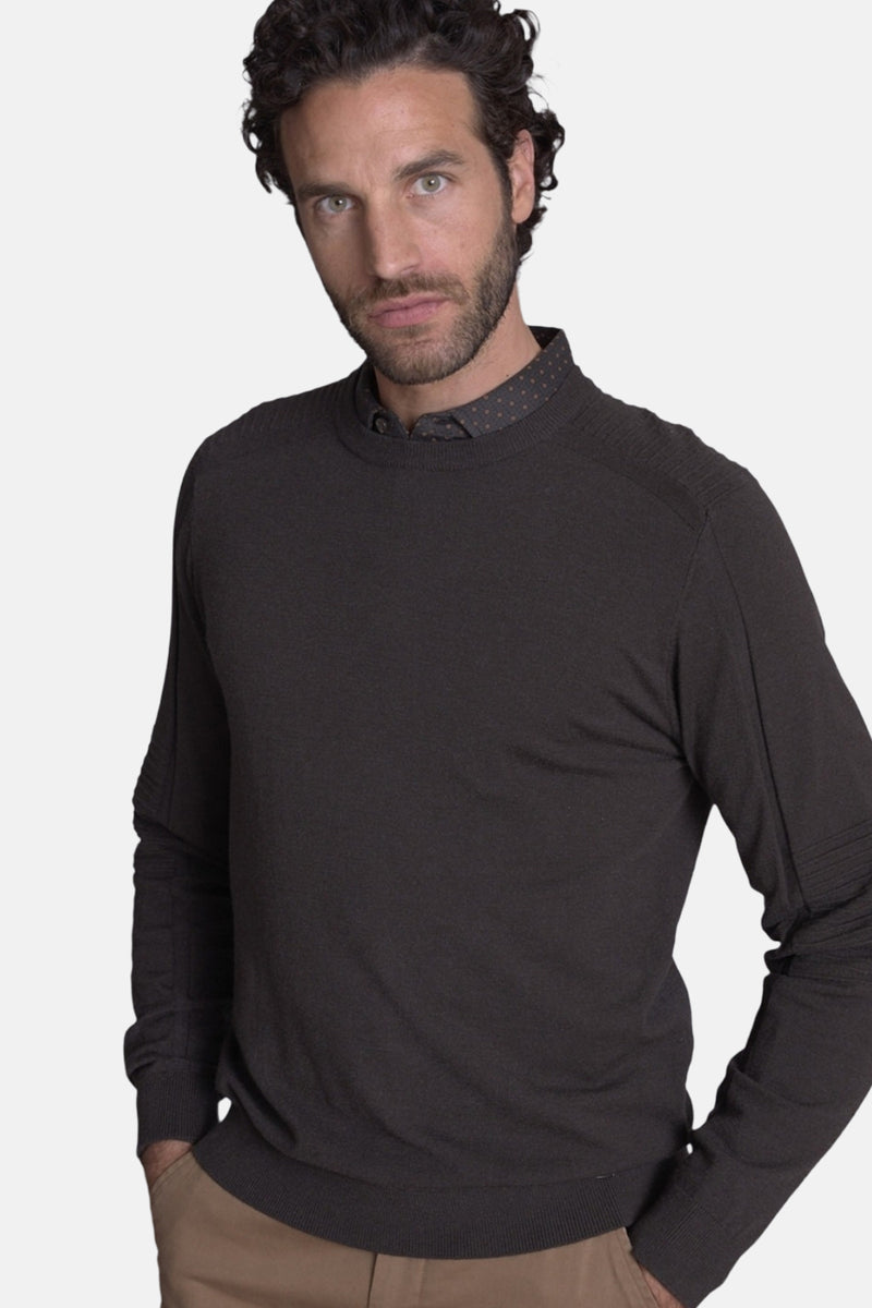 Pull col rond brun de DELAHAYE, porté avec une chemise à pois et un pantalon beige.