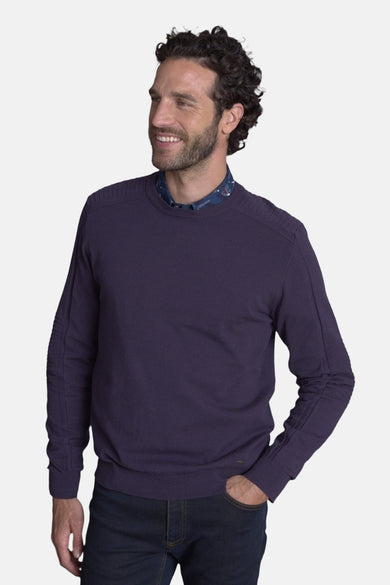 Pull col rond mauve de DELAHAYE, porté sur une chemise à motifs discrets et un jean foncé.
