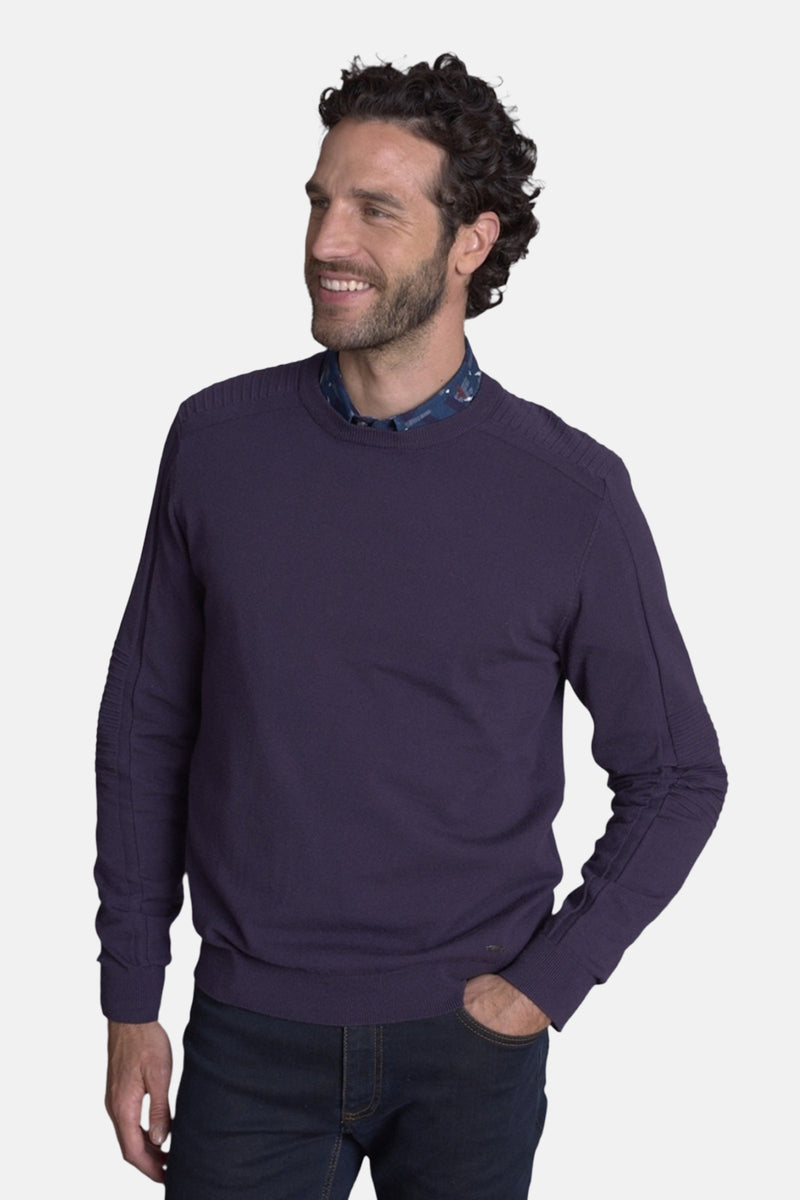 Pull col rond mauve de DELAHAYE, porté sur une chemise à motifs discrets et un jean foncé.
