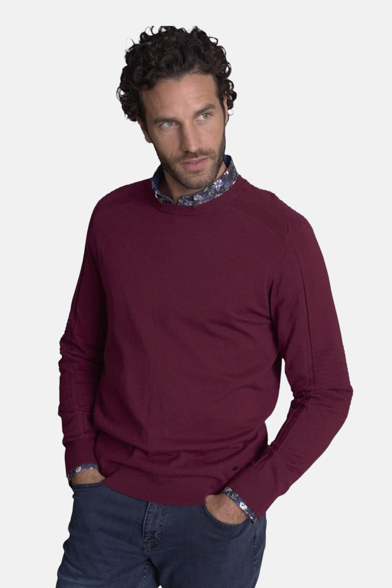 Pull col rond bordeaux de DELAHAYE, porté sur une chemise à motifs, avec un jean.