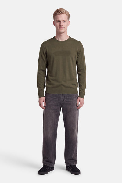 Pull vert en maille fine par DELAHAYE, col rond, manches longues, vue frontale sur modèle portant jeans gris foncé et baskets noires
